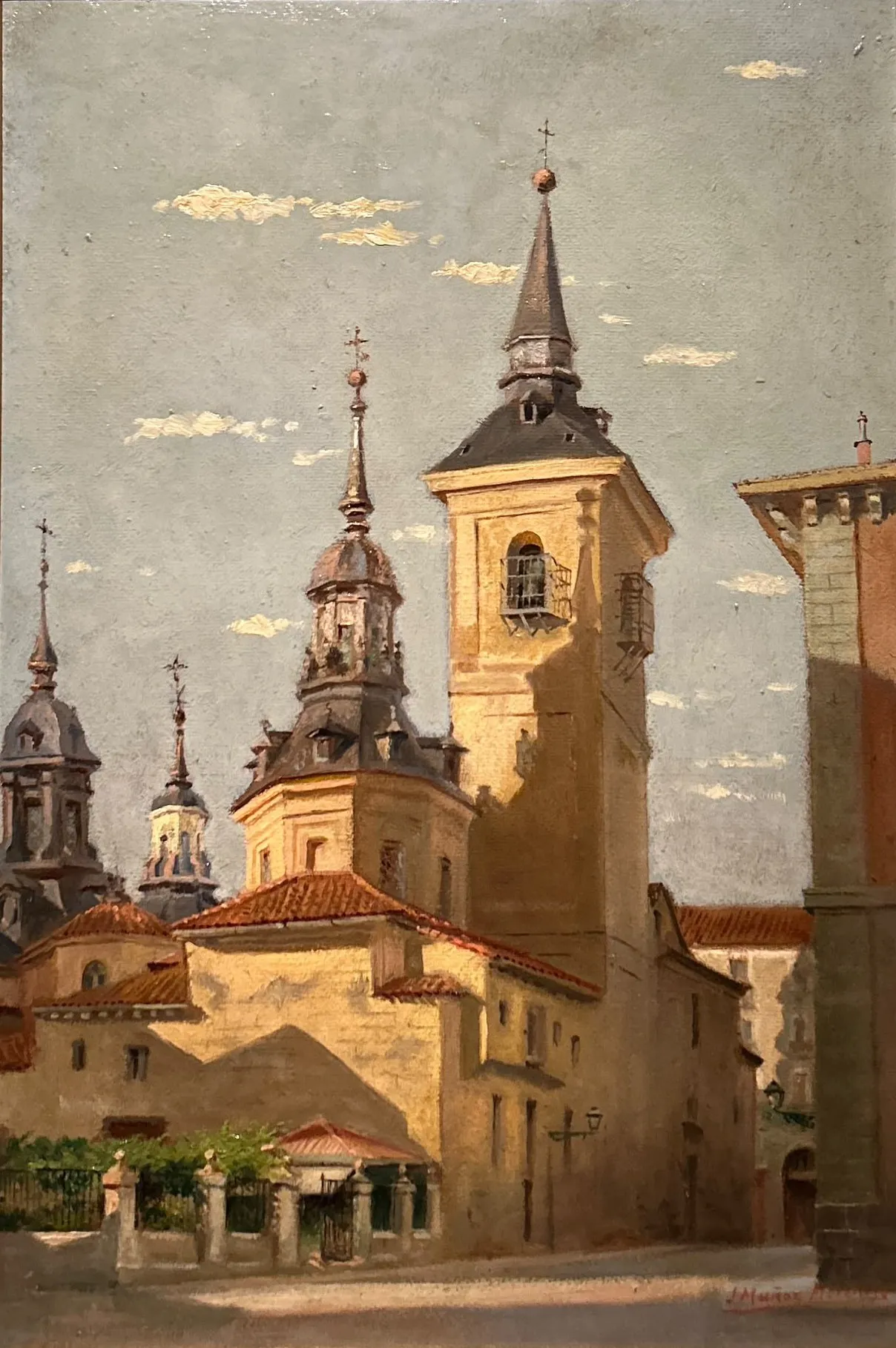 Óleo de una iglesia madrileña con su torre de chapitel, cúpulas al fondo y un jardín con verja en primer término, bañada por la luz de la tarde